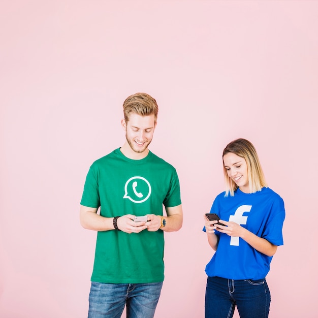 Sorrindo, homem jovem, e, mulher, usando, cellphone, sobre, cor-de-rosa, fundo