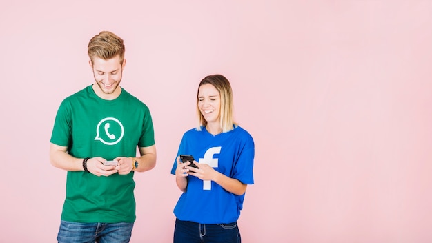 Sorrindo, homem jovem, e, mulher, usando, cellphone, sobre, cor-de-rosa, fundo