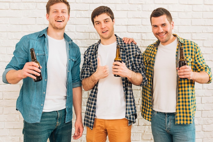 Foto grátis sorrindo, homem jovem, segurando, garrafa cerveja, em, mão, ficar, com, seu, amigo, mostrando, polegar cima, sinal