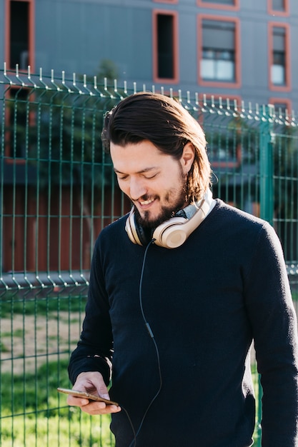 Sorrindo, homem jovem, usando, telefone móvel, com, headphone, ao redor, seu, pescoço