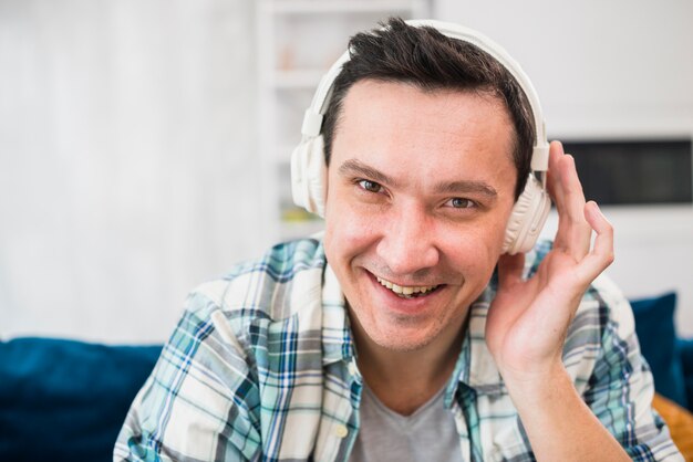 Sorrindo homem ouvindo música em fones de ouvido no sofá