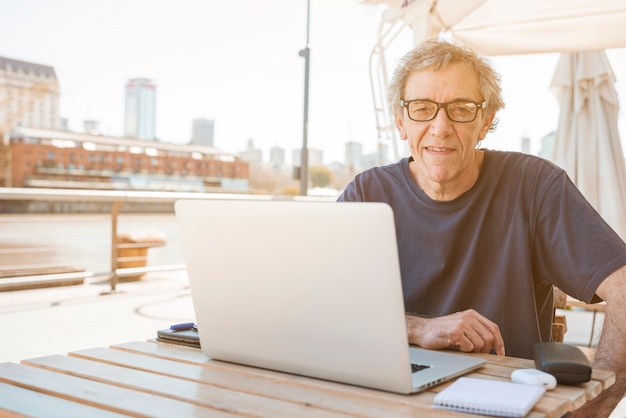 Sorrindo, homem sênior, sentando, em, restaurante, com, laptop, ligado, tabela