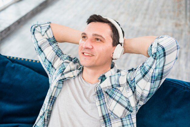 Sorrindo homem sonhador escuta música em fones de ouvido no sofá