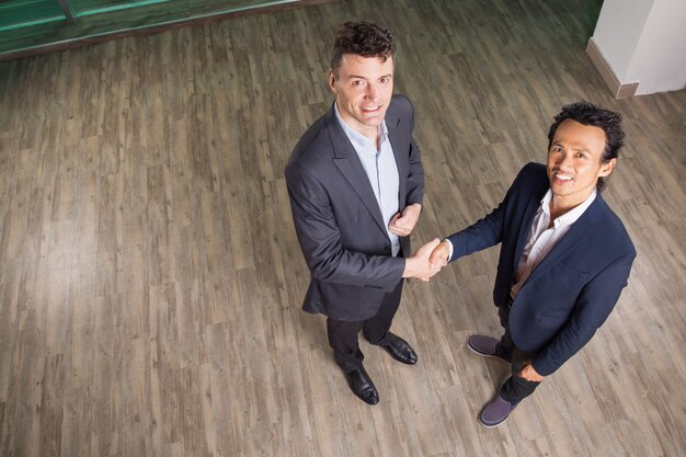 Foto grátis sorrindo homens de negócio que agitam as mãos no escritório salão