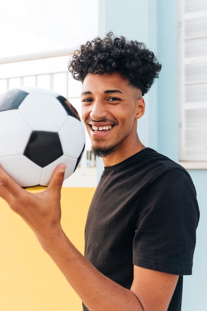 Sorrindo, jogador de futebol, segurando bola, e, olhando câmera