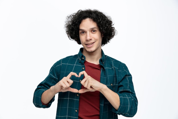 Foto grátis sorrindo jovem bonito fazendo sinal de coração enquanto olha para a câmera isolada no fundo branco