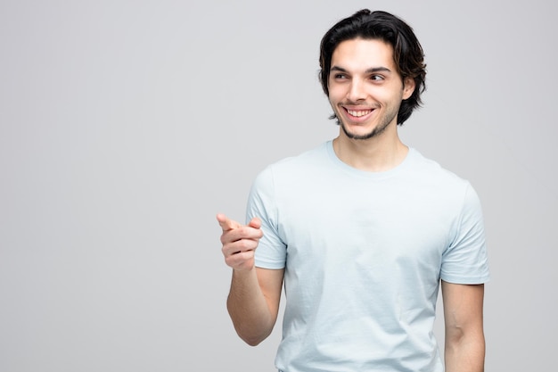 sorrindo jovem bonito olhando e apontando para o lado isolado no fundo branco com espaço de cópia