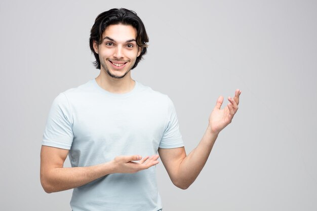 sorrindo jovem bonito olhando para a câmera apontando para o lado com as mãos isoladas no fundo branco