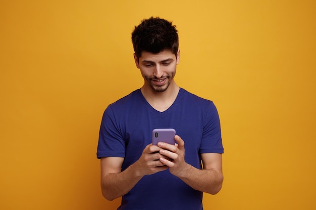 Sorrindo jovem bonito usando seu celular em fundo amarelo