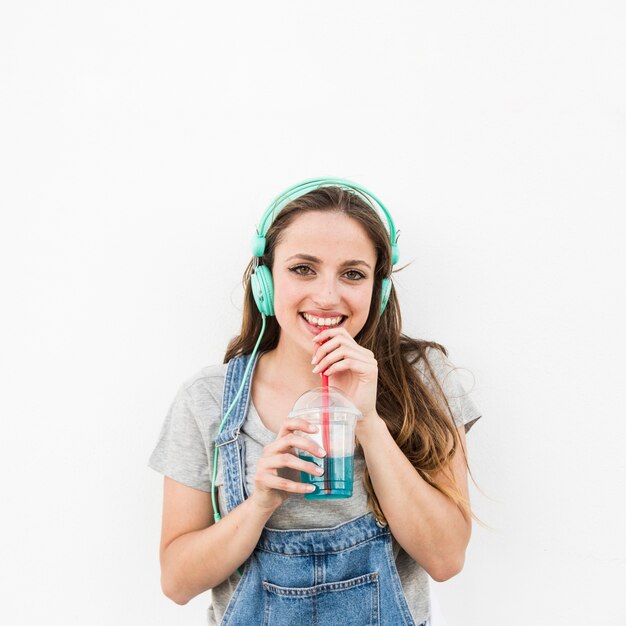 Sorrindo jovem com fone de ouvido na cabeça dele bebendo suco