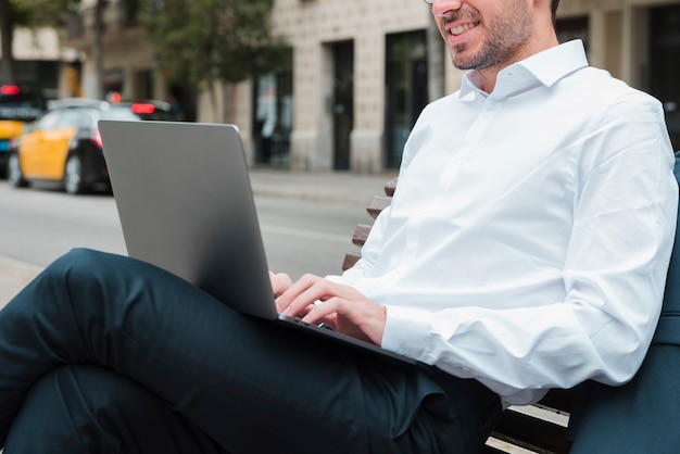 Sorrindo, jovem, homem negócios, sentar-se banco, usando computador portátil