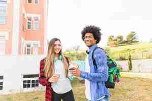 Foto grátis sorrindo, jovem, macho fêmea, estudantes, segurando, taqui, xícara café, e, livros, em, mão, ficar, em, campus