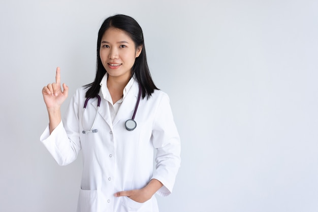 Sorrindo jovem médico feminino levantando o dedo indicador