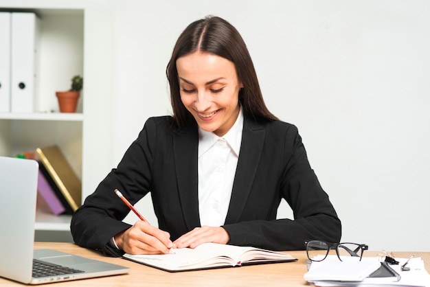 Sorrindo, jovem, mulher, escrita, diário, lápis, escritório, escrivaninha