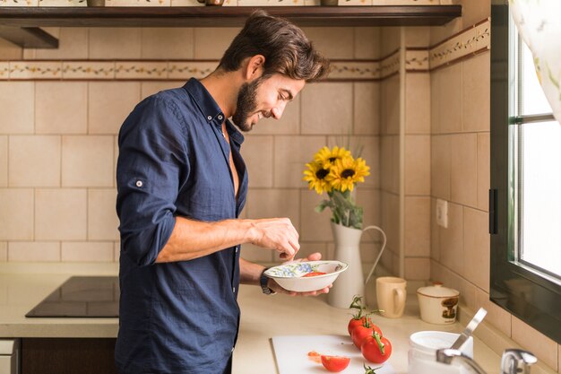 Sorrindo jovem preparando salada na cozinha