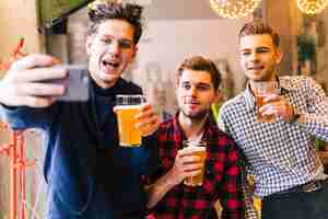 Foto grátis sorrindo jovens amigos do sexo masculino segurando os copos de cerveja tomando selfie no telemóvel