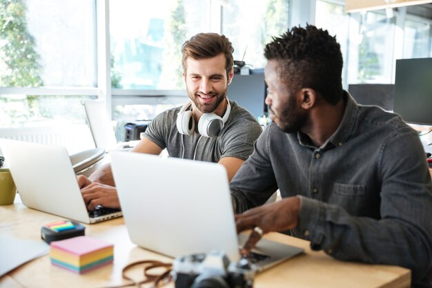 Sorrindo jovens colegas sentados no escritório de coworking usando laptop