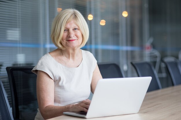 Sorrindo líder feminino sênior trabalhando em laptop