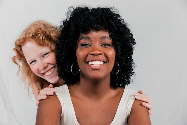 Sorrindo, loiro, mulher jovem, estar, atrás de, a, africano, amigo, contra, cinzento, fundo