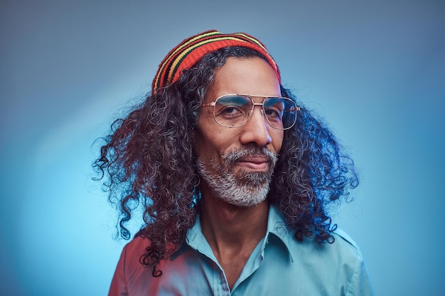 Foto grátis sorrindo macho rastafari africano vestindo uma camisa azul e gorro. retrato de estúdio em um fundo azul.