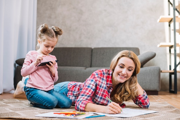 Sorrindo, mãe, livro desenho, com, dela, filha, usando, telefone móvel