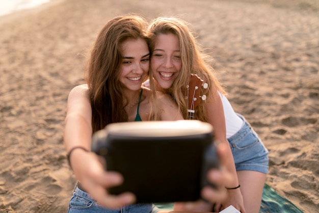 Sorrindo, meninas jovens, levando, auto-retrato, de, câmera instantânea, em, praia