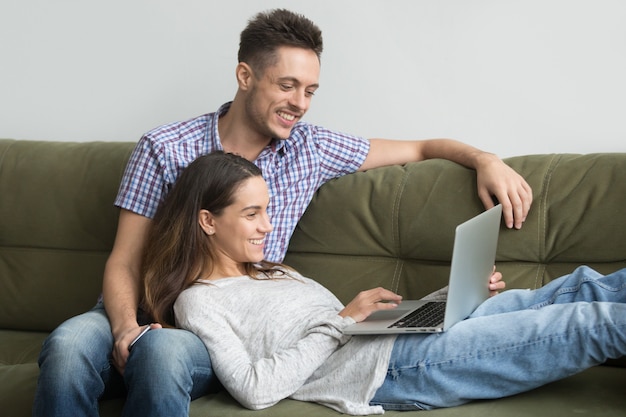 Sorrindo, millennial, par, desfrutando, usando computador portátil, relaxante, ligado, sofá, junto
