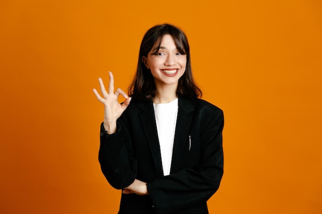 Sorrindo mostrando um gesto bem jovem linda mulher vestindo jaqueta preta isolada em fundo laranja