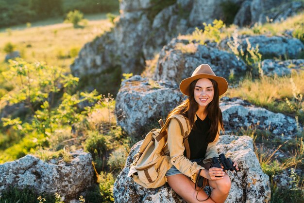 Sorrindo, mulher bonita, sentando, ligado, rocha, segurando, binocular