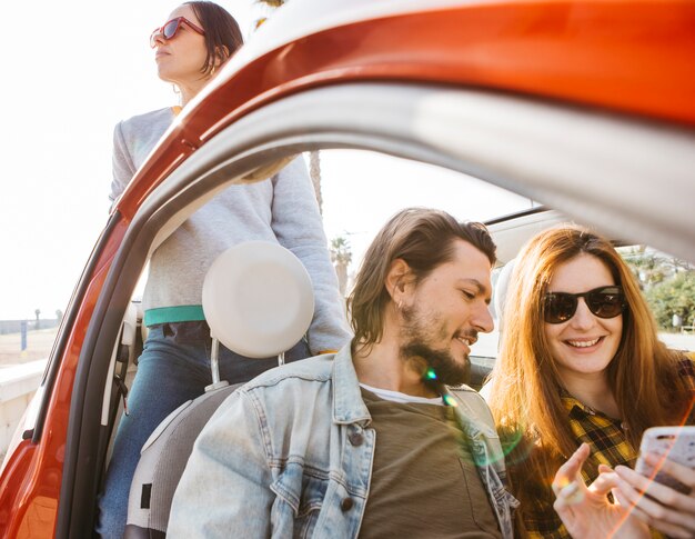 Sorrindo, mulher, e, positivo, homem olha, em, smartphone, carro, perto, senhora, inclinar-se, saída, de, automóvel