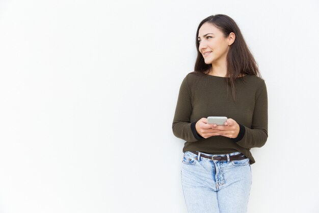 Sorrindo mulher focada segurando o celular e desviar o olhar