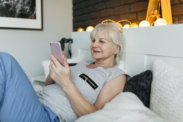 Sorrindo, mulher idosa, usando, smartphone, cama