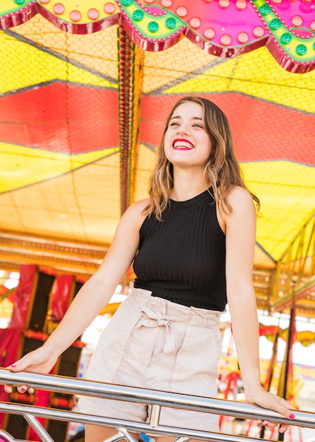 Sorrindo, mulher jovem, estar, atrás de, a, trilhos, em, parque divertimento