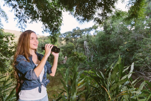 Sorrindo, mulher jovem, explorar, floresta, com, binóculos
