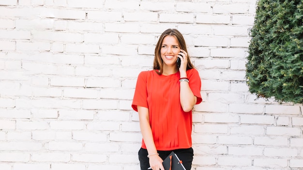 Sorrindo, mulher jovem, falando, ligado, smartphone, frente, parede tijolo