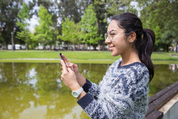 Sorrindo, mulher jovem, usando, smartphone, parque