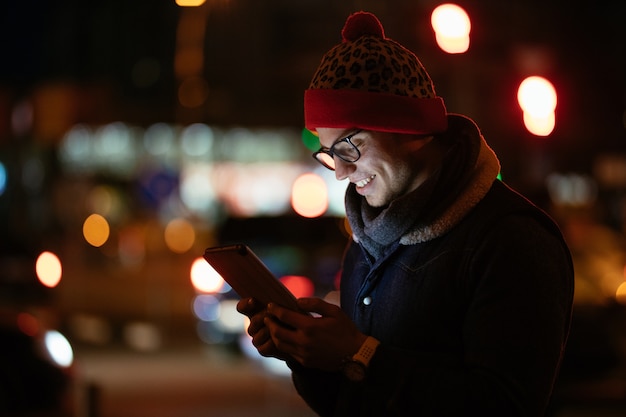 Sorrindo na moda homem de óculos usando seu telefone celular