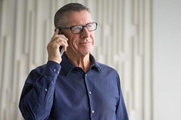 Sorrindo O homem de negócios sênior que fala no Smartphone