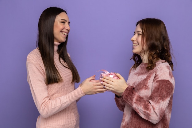 Sorrindo, olhando uma para a outra, duas garotas segurando presentes