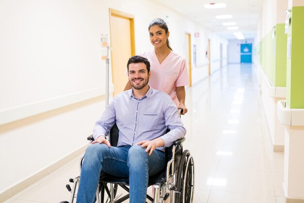 Sorrindo ordenadamente empurrando paciente adulto médio em cadeira de rodas no corredor do hospital