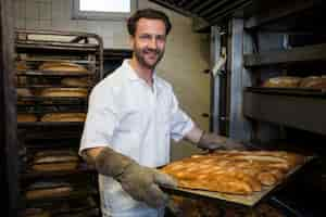 Foto grátis sorrindo padeiro remover bolos cozidos do forno