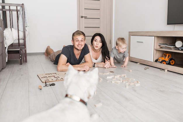 Foto grátis sorrindo, par jovem, mentindo, ligado, assoalho hardwood, com, seu, filho, olhar, cachorro branco