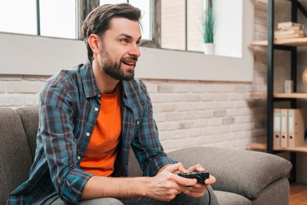 Sorrindo, retrato, de, um, homem jovem, sentar sofá, jogando videogame