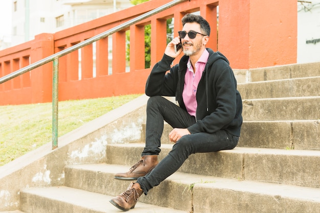 Sorrindo, retrato, de, um, homem moderno, sentando, ligado, escadaria, conversa telefone móvel