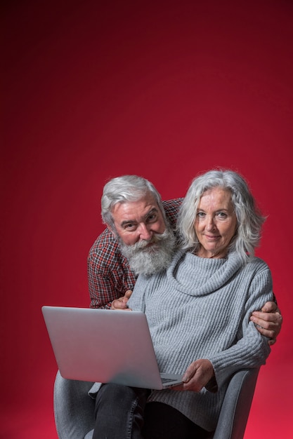 Sorrindo, retrato, de, um, homem sênior, abraçar, dela, esposa, detrás, sentando, ligado, cadeira, com, laptop