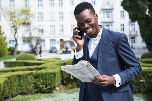 Sorrindo, retrato, de, um, jovem, homem negócios, falando telefone móvel, lendo jornal