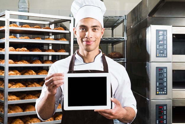 Sorrindo, retrato, de, um, macho, padeiro, em, uniforme, segurando, pequeno, em branco, tablete digital, em, panificadora