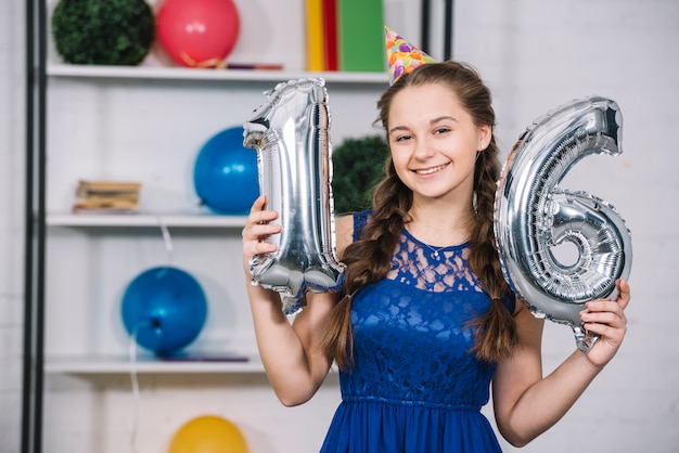 Foto grátis sorrindo, retrato, de, um, menina aniversário, segurando, numeral, 16, folha, prata, balloon