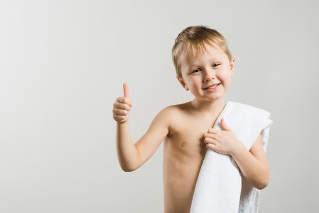 Sorrindo, retrato, de, um, shirtless, loiro, menino, com, branca, toalha, ligado, ombro, mostrando, polegar cima, sinal, contra, experiência cinza