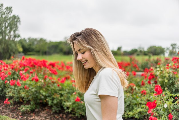 Sorrindo, senhora, em, t-shirt, perto, flores vermelhas